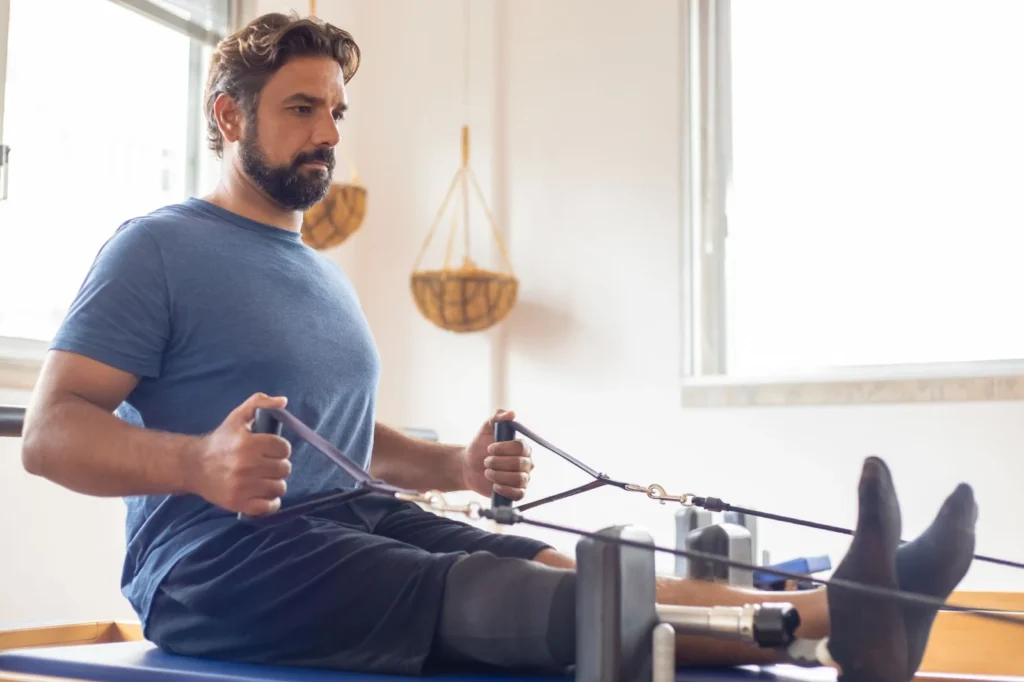 Man with prosthetic leg performing pilates rehabilitation indoors, focusing on strength and recovery.